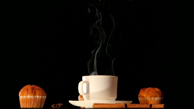 White steaming coffee cup with cakes, anise, cinnamon on black