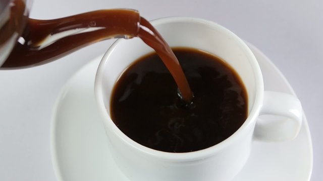 Pouring coffee into a cup on white background, slow motion