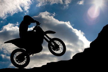 Fototapeta na wymiar Motocross - silhouette with a rock and blue sky with sun