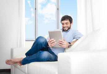 Young Hispanic man at home on couch using digital tablet