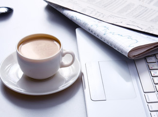 Cup of coffee near the laptop and newspapers