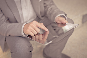 Obraz premium Businessman using electronic tablet pc. He is sitting on a stair