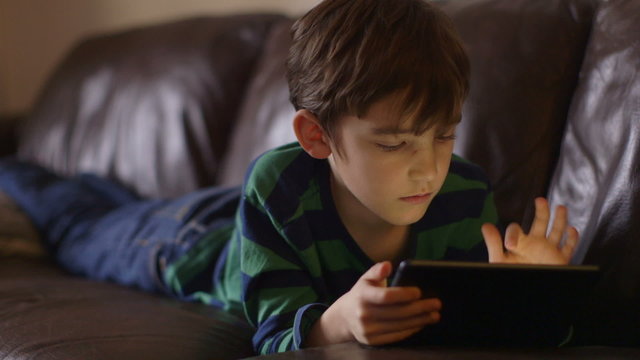 Young boy engrossed in playing games on a touchscreen tablet on a sofa