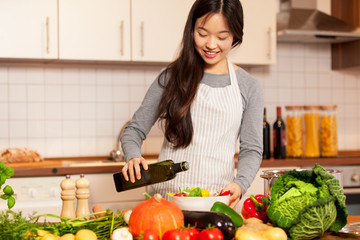 Asian smiling woman is pouring olive oil into the colorful salad