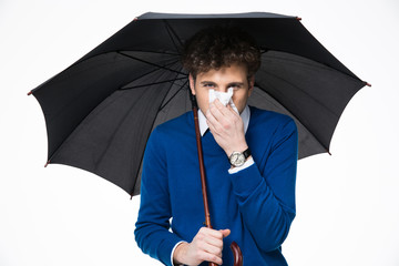 Sick business man holding umbrella and blowing nose