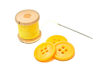 buttons and spool of yellow thread on white