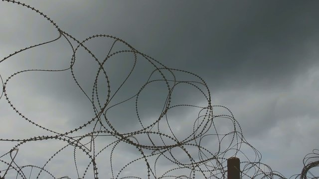 Barbed wire on the dark stormy clouds background. Time lapse