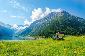 A young woman sits on bench beside an azure mountain lake