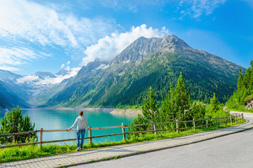 A young woman stands beside an azure mountain lake, Alps