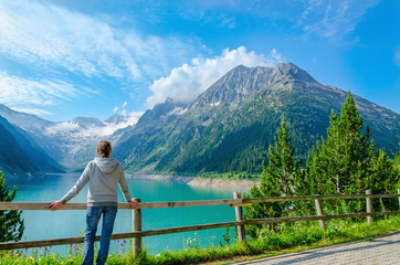 Fototapeta na wymiar A young tourist stands beside an azure mountain lake