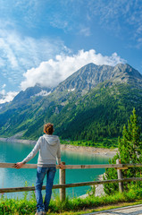 A young tourist stands beside an azure mountain lake