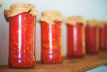 Canned tomatoes in glass jars on wooden shelf.
