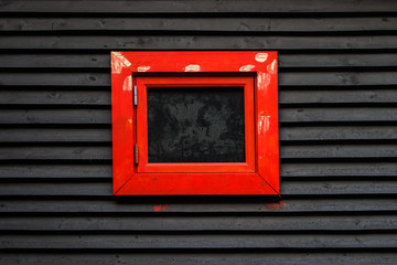 Obraz na płótnie Canvas black sheathed wooden wall with red framed window
