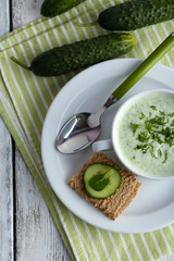 Cucumber soup in bowl on color wooden table background