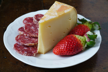 Fontina, salame e fragole su piatto tavolo e sfondo nero