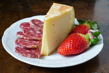 Fontina, salame e fragole su piatto tavolo e sfondo nero