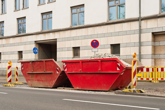 Zwei rote Container f&uuml;r Bauschutt stehen am Strassenrand
