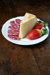 Fontina, salame e fragole su piatto tavolo e sfondo nero
