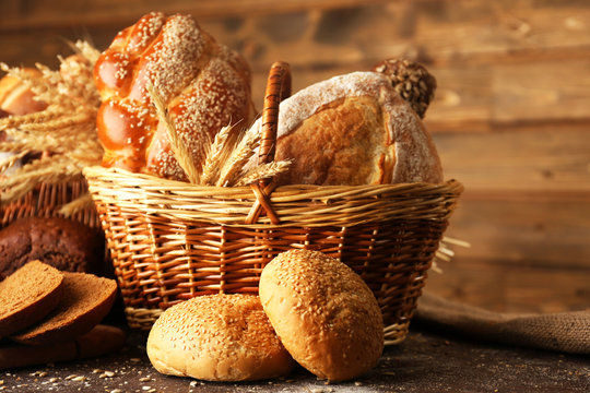 Different bread with ears in basket on wooden background