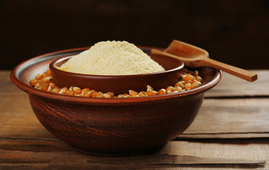 Flour and corn grains in bowls with spoon on wooden background