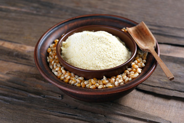 Flour and corn grains in bowls with spoon on wooden background