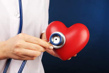 Doctor hands with heart and stethoscope on blue background