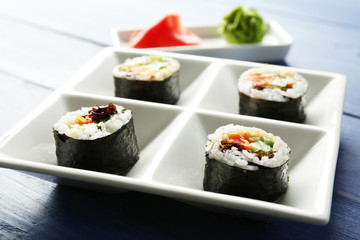 Vegetable sushi rolls on plate on color wooden background