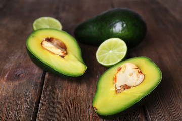Sliced avocado with pieces of lime on wooden background