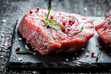 Piece of meat with rosemary and pepper on a stone plate