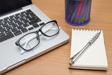 Blank business laptop, pen, note and glasses on wooden table