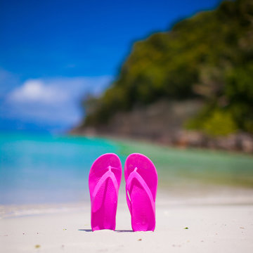 Pink vibrant beach flip flops on white sand on sea background