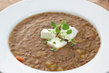 Plate of lentil soup with feta cheese cubes and fresh oregano.