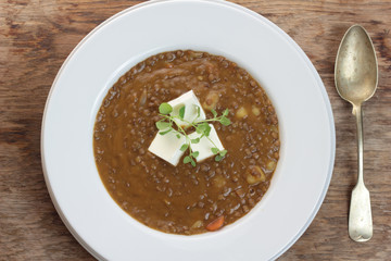 Plate of lentil soup with feta cheese cubes and fresh oregano.