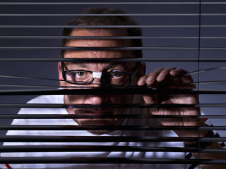 Vicious man looking sideways through venetian blind