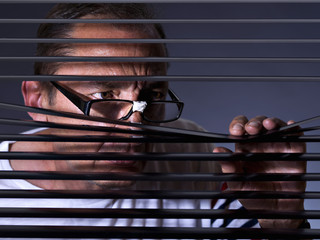 Vicious man looking sideways through venetian blind