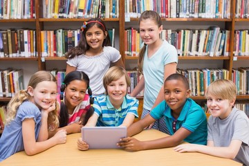 Fototapeta na wymiar Cute pupils using tablet computer in library