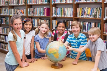 Cute pupils looking at globe in library