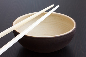Empty rustic ceramic bowl with chopsticks. On dark surface.