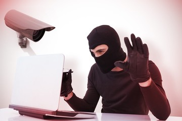 Composite image of focused burglar hacking into laptop