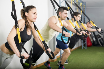 People at gym doing trx elastic rope exercises