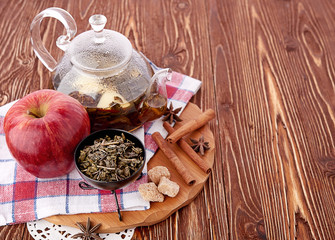 Ripe apple, cinnamon and fruit drink in glass teapot on wooden