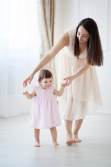 Fototapeta na wymiar little girl first steps with the help of mom
