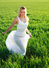 Romantic woman in white dress running across green field