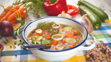 Vegetable soup in a metal bowl on a rural rustic wooden table.