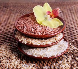 Different types of rice in bowls on wicker background