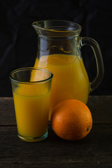 Jug and glass with fresh orange juice, still life art on dark ba