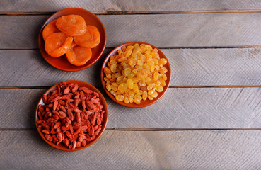 Dried fruits in small plates on wooden planks background