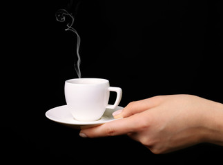 Female hand holding cup of coffee on black background