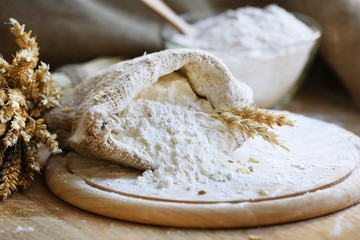 Fototapeta na wymiar Flour in burlap bag on cutting board and wooden table