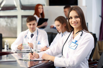 Fototapeta premium Beautiful young doctor with team in conference room
